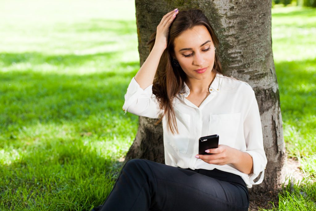 girl works with her phone sitting tree